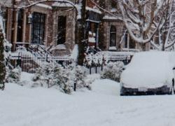 Photograph of a street, the road an cars are covered in snow.