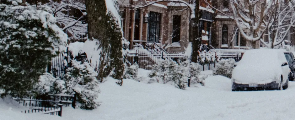 Photograph of a street, the road an cars are covered in snow.