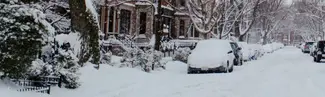 Photograph of a street, the road an cars are covered in snow.